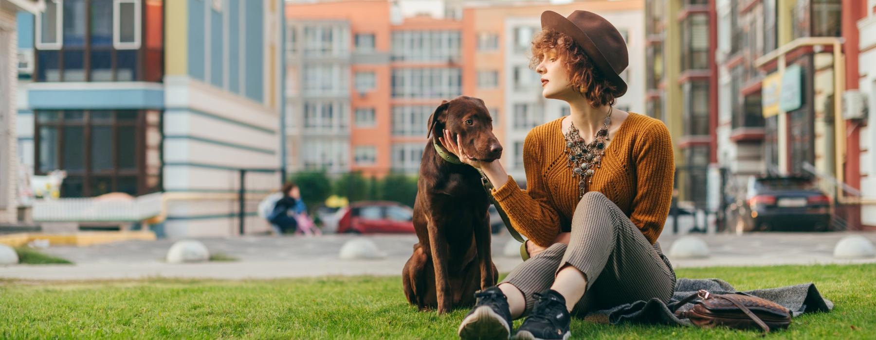 a person and a dog sitting on grass by buildings